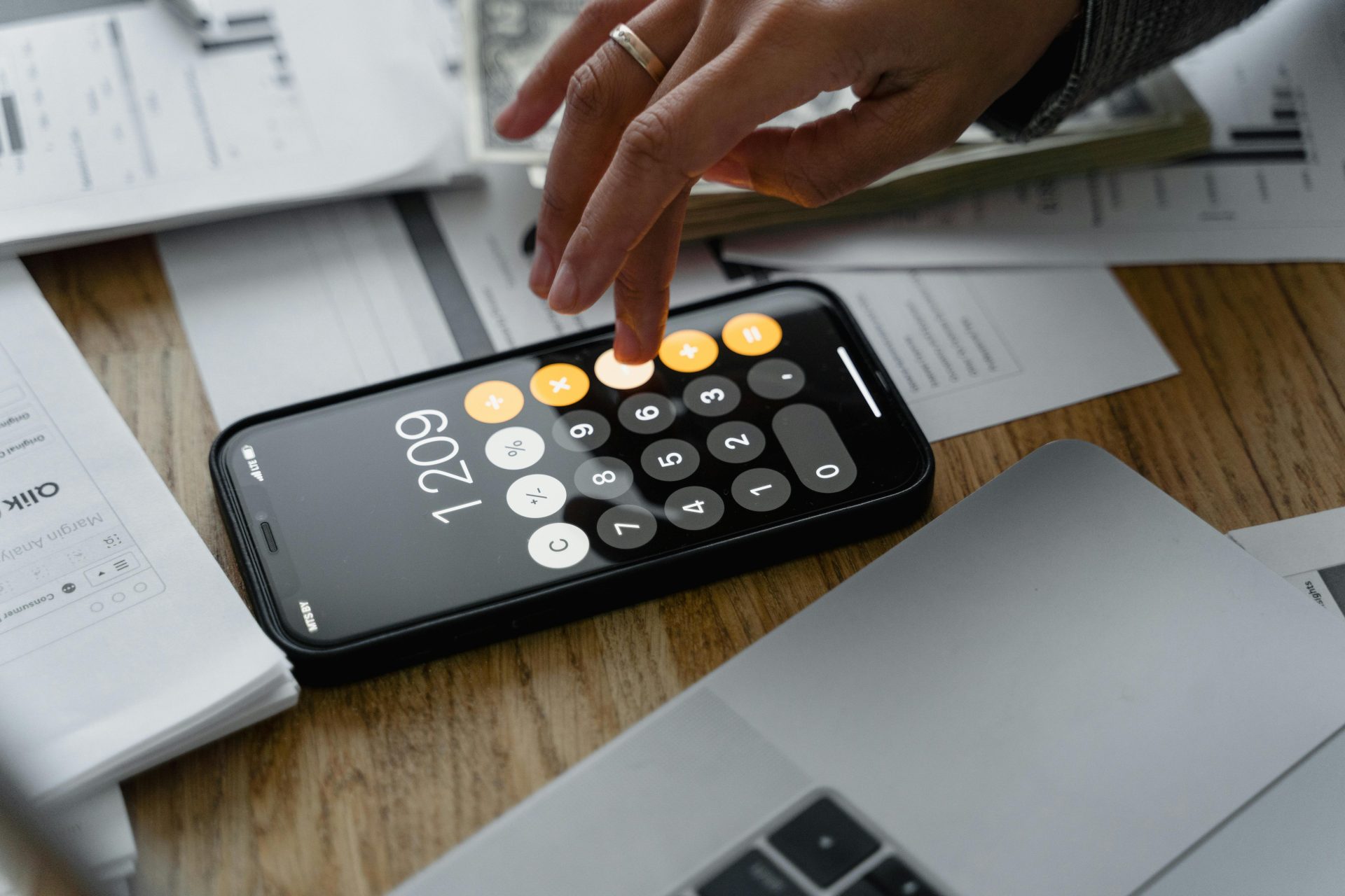 Gros plan d'une personne utilisant une calculatrice pour smartphone sur une table avec des documents pour des calculs financiers.