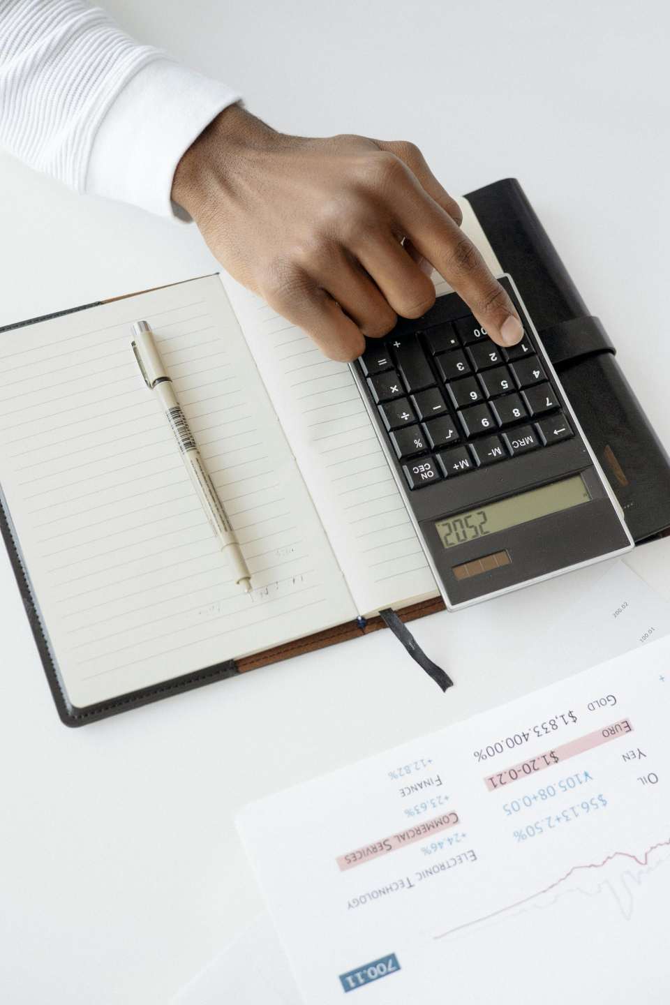 Une main utilisant une calculatrice avec des documents financiers et un cahier, représentant un bureau aménagé pour l'analyse financière.