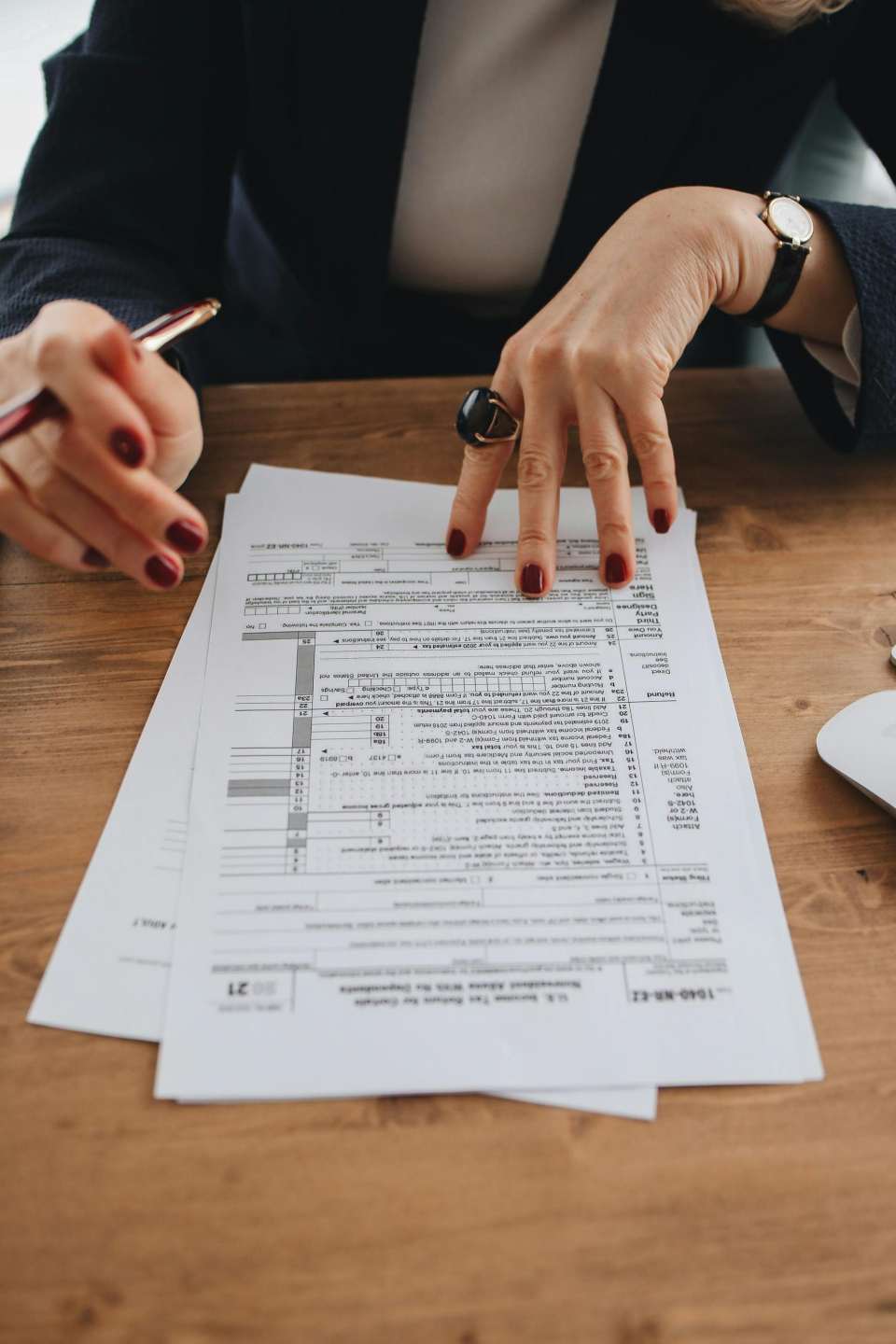 Mains aux ongles manucurés examinant des formulaires fiscaux sur une table en bois à l'intérieur.