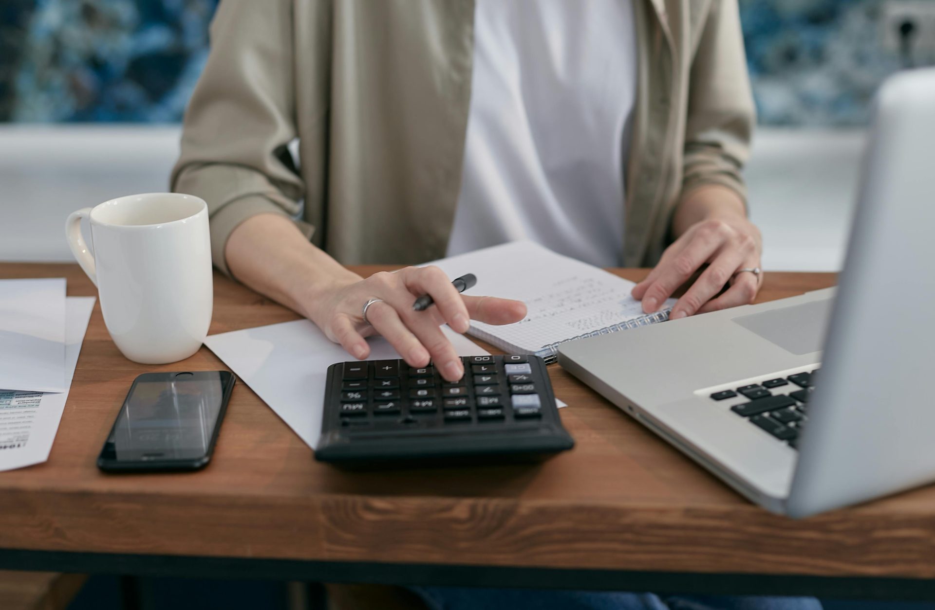 Une personne utilisant une calculatrice et un ordinateur portable tout en prenant des notes sur un bureau en bois.
