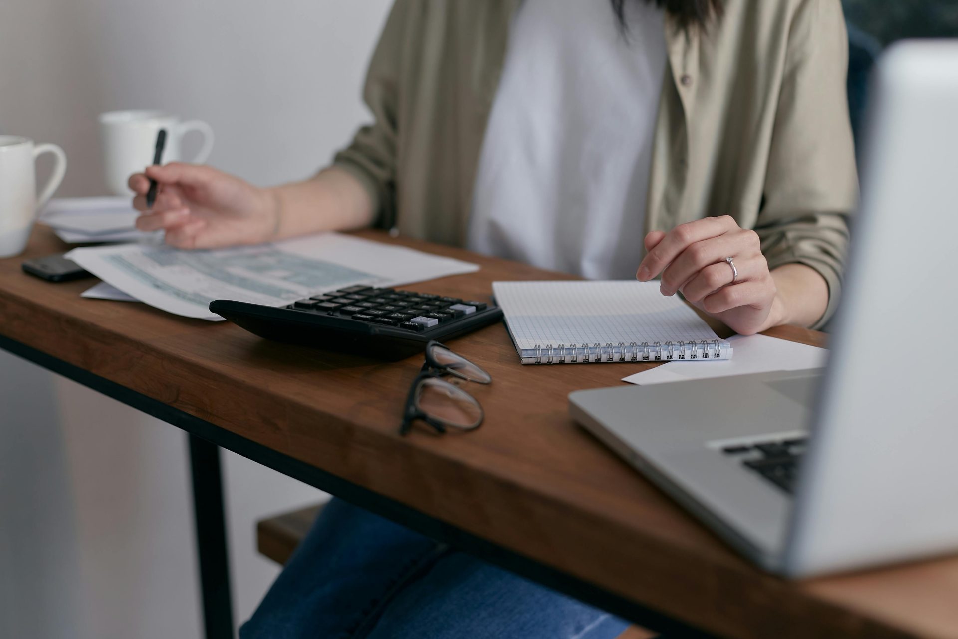 Une femme gère ses finances à la maison, à l'aide d'un ordinateur portable et d'une calculatrice sur un bureau en bois.