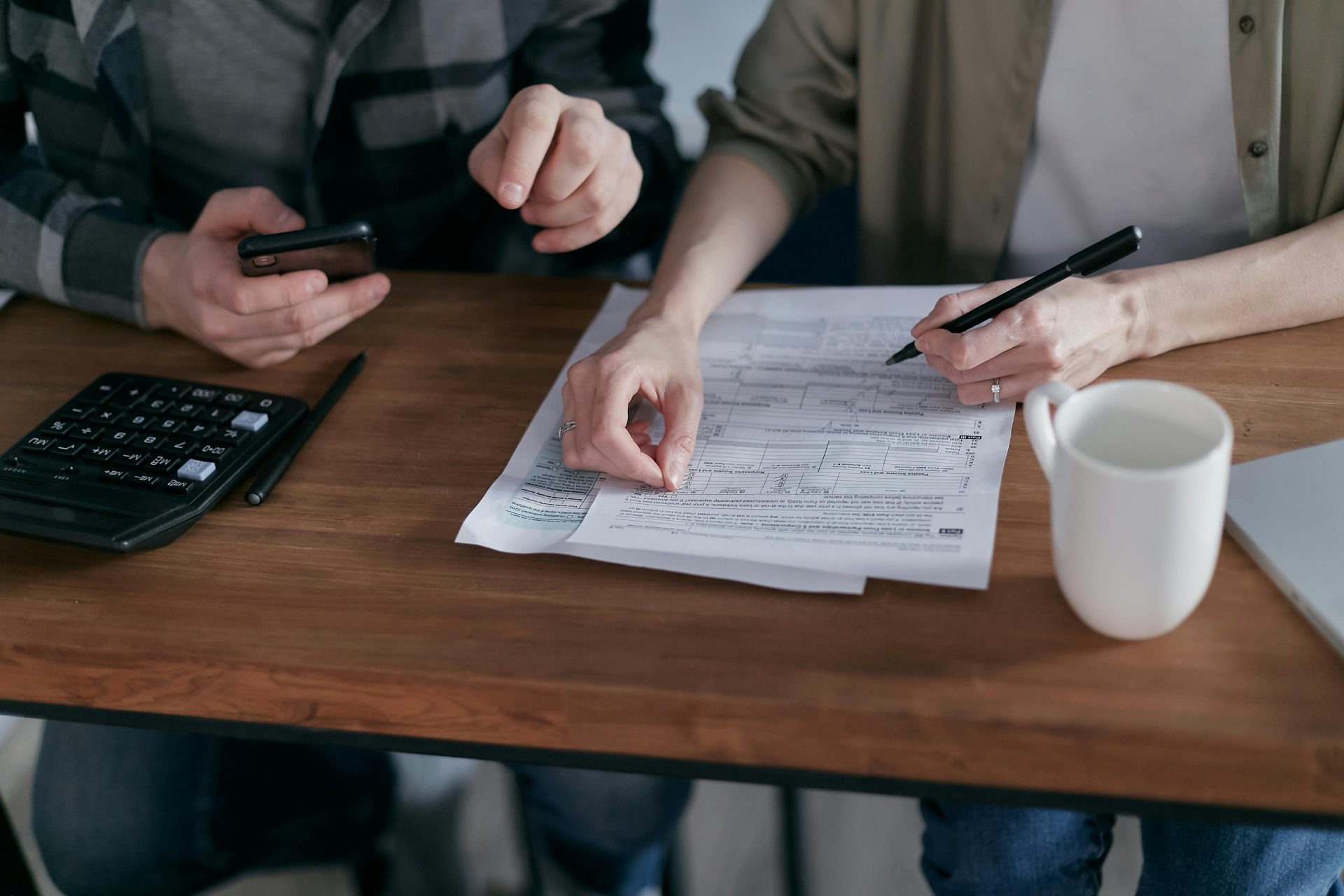 Couple gérant ses finances à la maison avec une calculatrice, un smartphone et des documents.