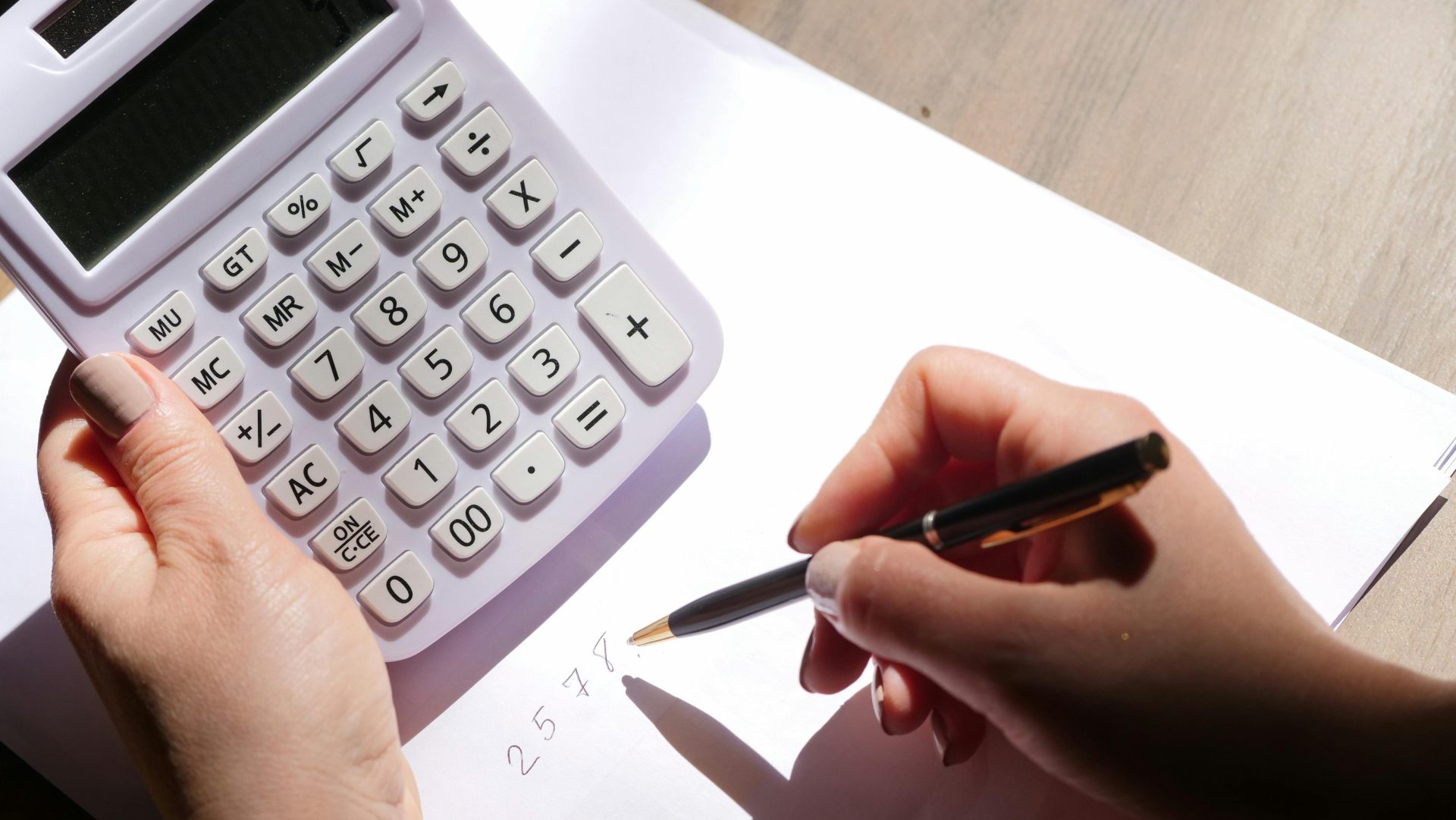 Mains utilisant une calculatrice et écrivant des chiffres sur du papier sous la lumière du soleil. Idéal pour les thèmes de la finance et de l'éducation.