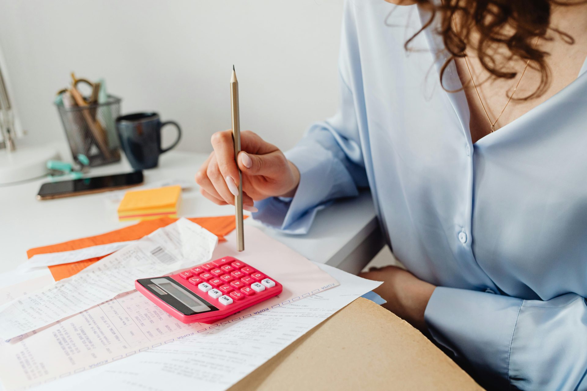 Une femme calcule ses dépenses à l’aide d’une calculatrice et de papiers posés à son bureau.