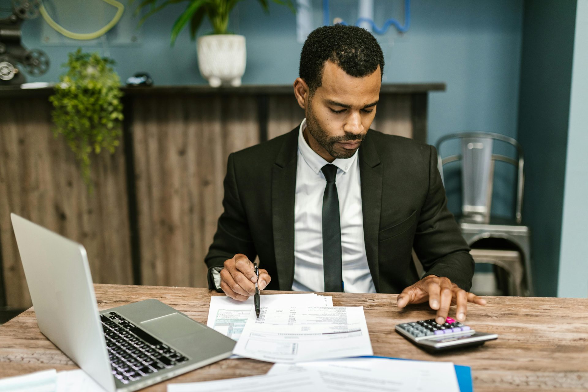 Un homme d’affaires concentré travaille avec une calculatrice et des documents dans un bureau moderne.