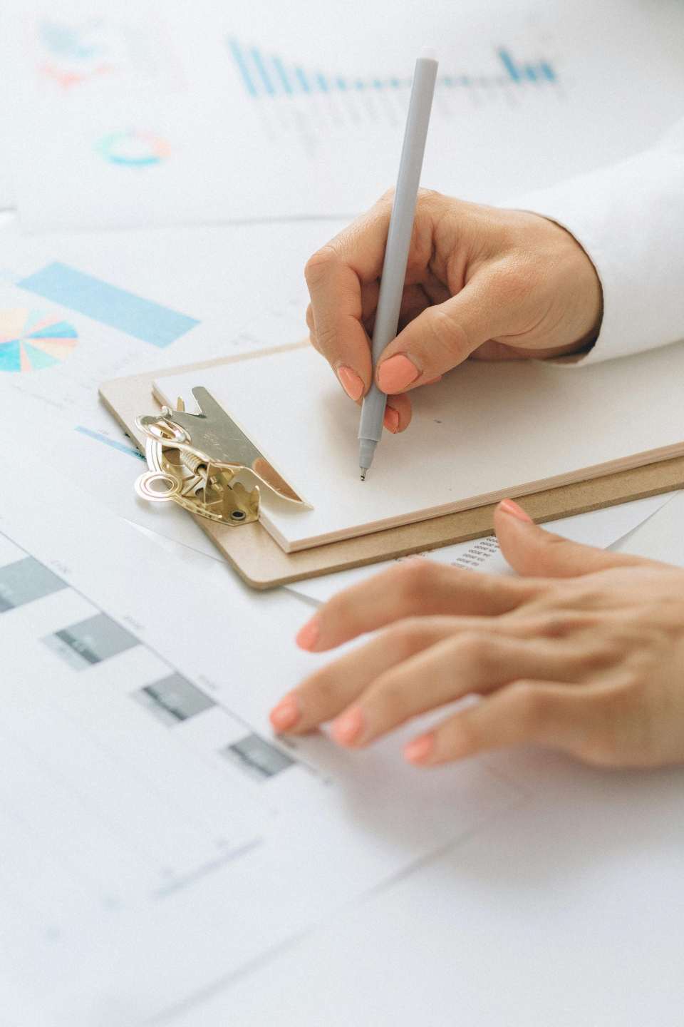 Détail de mains écrivant avec un stylo sur un presse-papiers au-dessus de documents financiers.