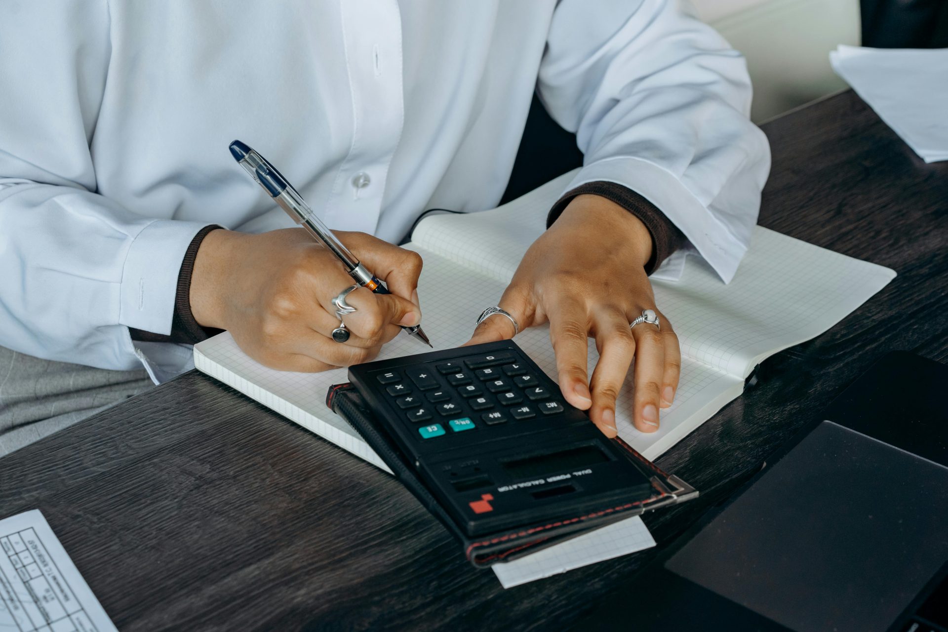 Gros plan d'un professionnel écrivant des notes avec une calculatrice sur un bureau en bois.