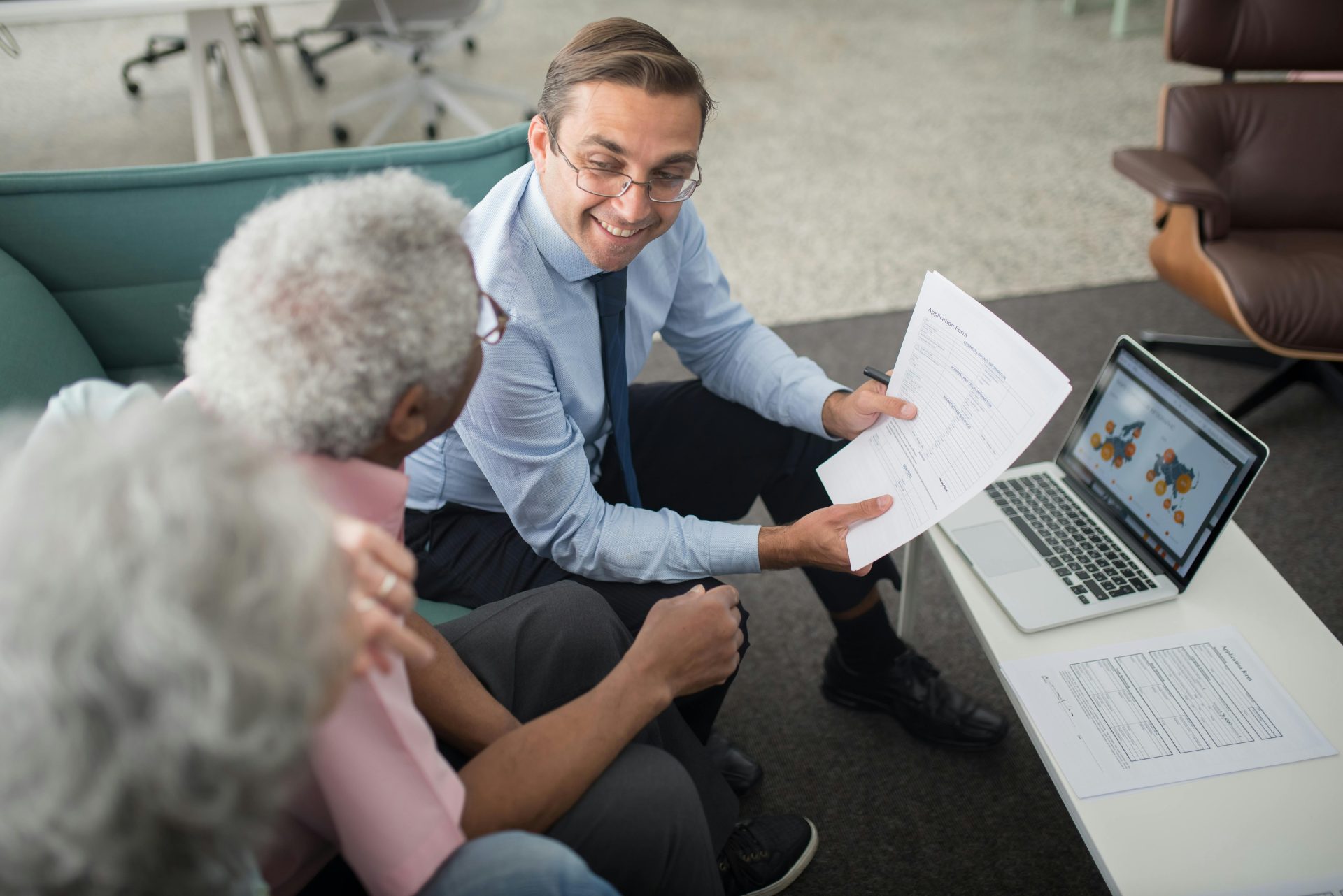 Un conseiller financier discute de documents avec des clients seniors dans un bureau, présentant une séance de consultation collaborative.